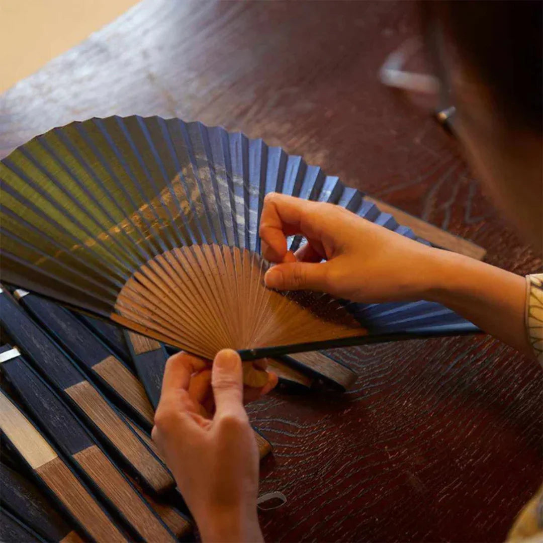 Artisan crafting a traditional Japanese hand fan with wooden ribs on a wooden table