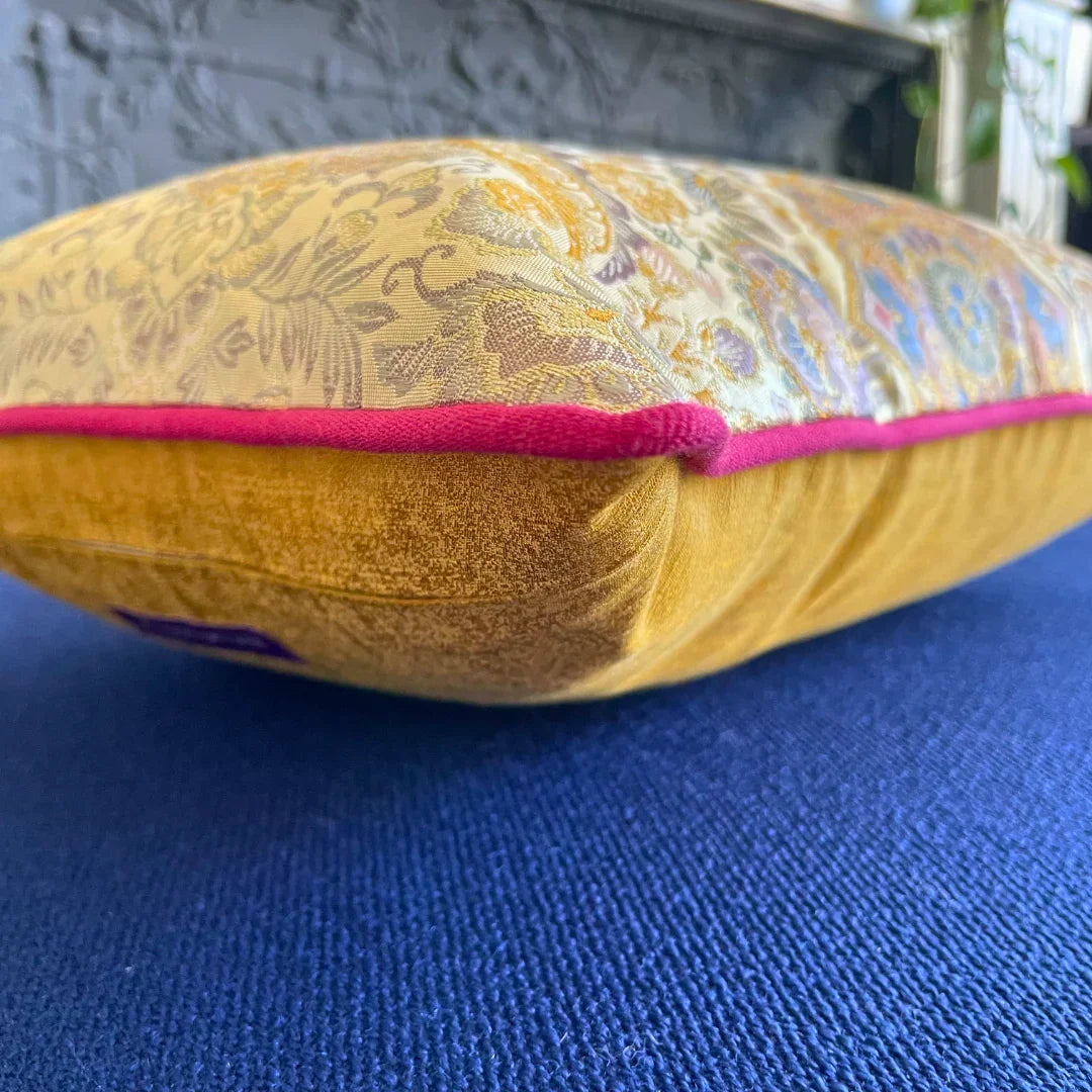 Vintage obi-kimono cushion with gold floral pattern, pink trim, on blue fabric surface