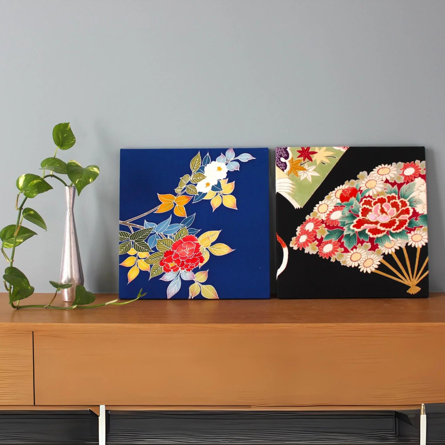 Two vintage Obi Kimono cushions with floral patterns on a wooden sideboard, plant in vase.